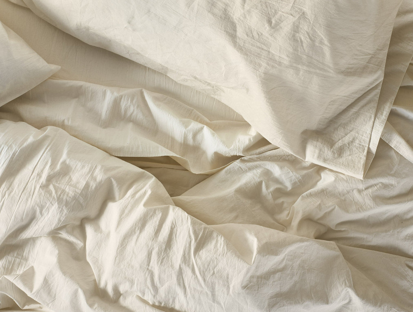 Close-up of crinkled ivory percale fabric with soft natural shadows and texture.