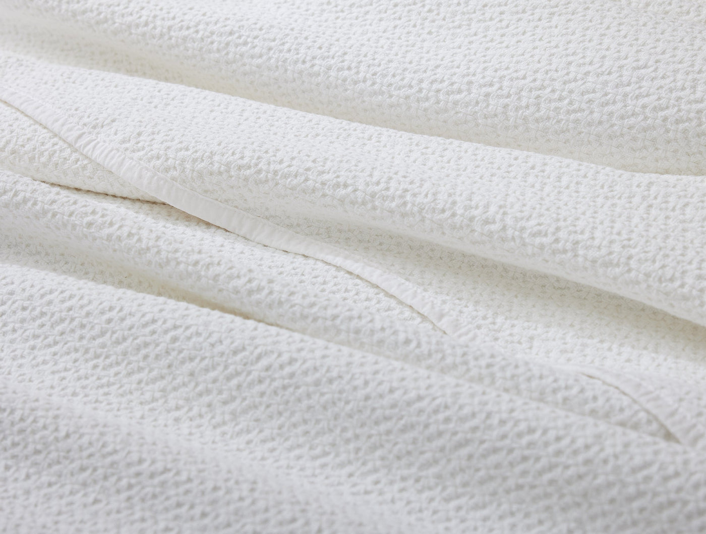 Close-up of Coyuchi Honeycomb blanket in white, showing textured waffle-weave fabric detail.