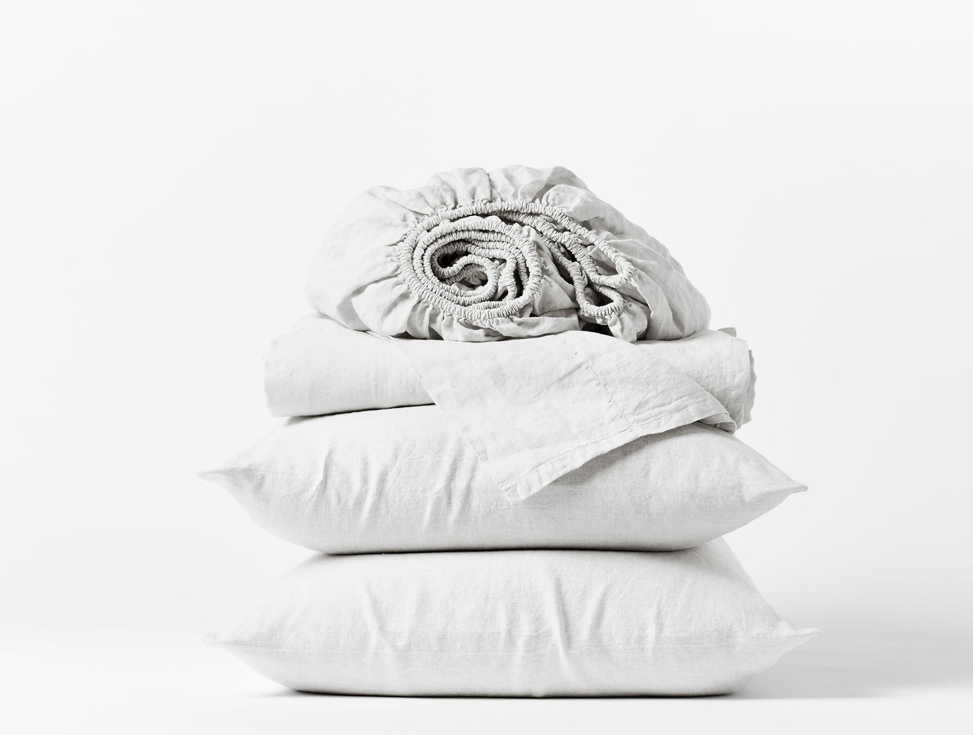 Coyuchi Relaxed Linen sheet set in white, folded stack with pillowcases and rolled fitted sheet.