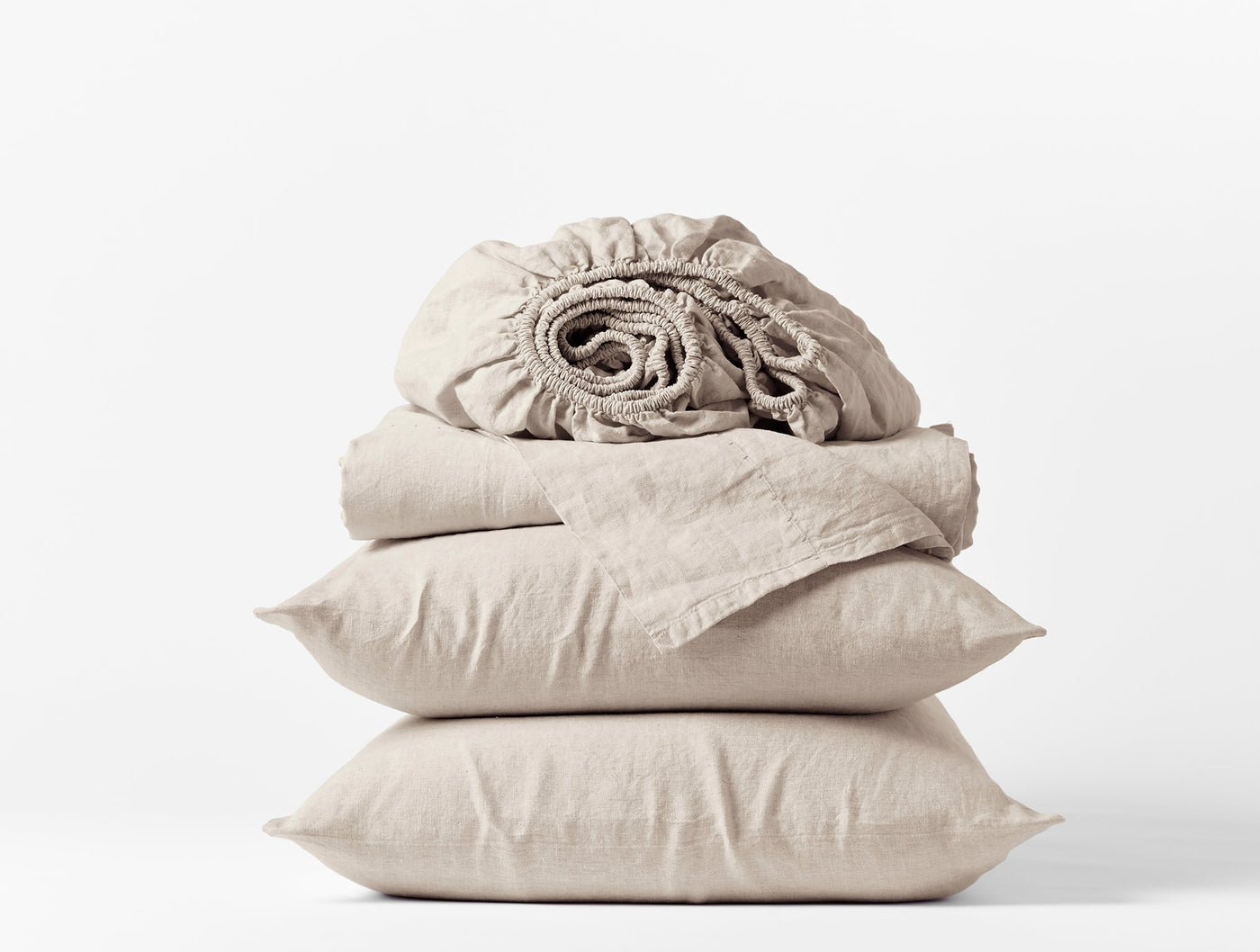 Close-up of stacked natural linen sheet set with pillowcases and rolled fitted sheet.