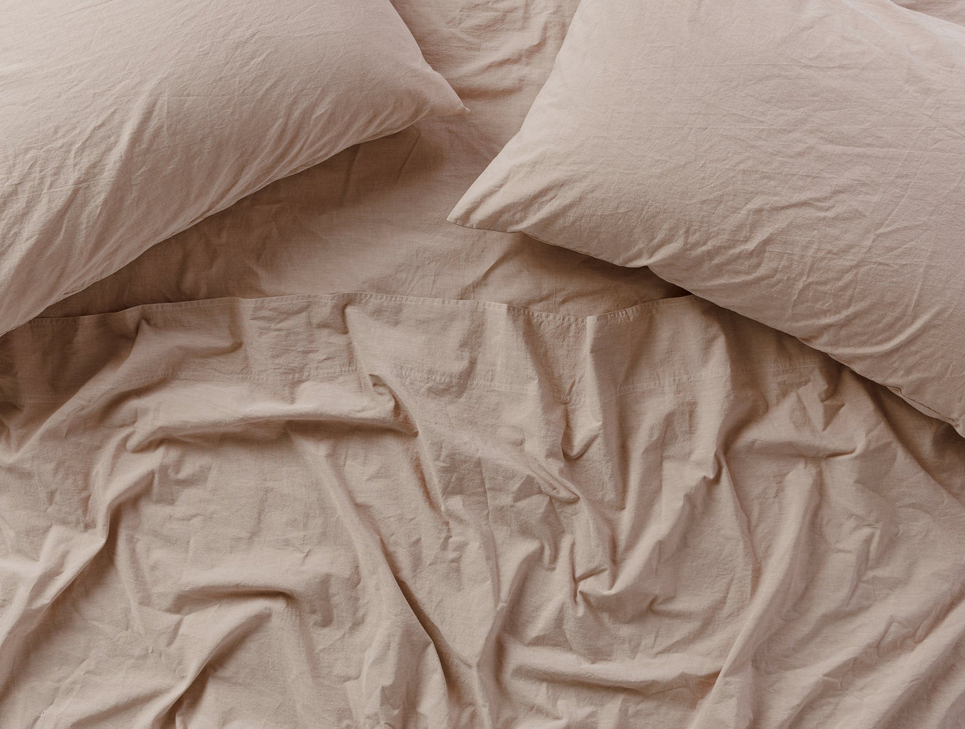Blush crinkled percale pillowcases styled on a bed, overhead view showing relaxed texture.