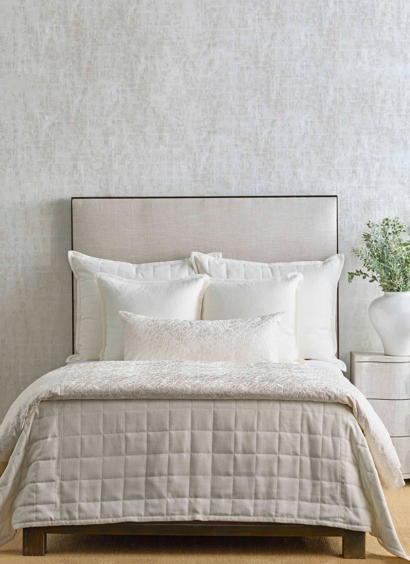 Ivory embroidered duvet cover styled on bed with quilted champagne coverlet and layered pillows.