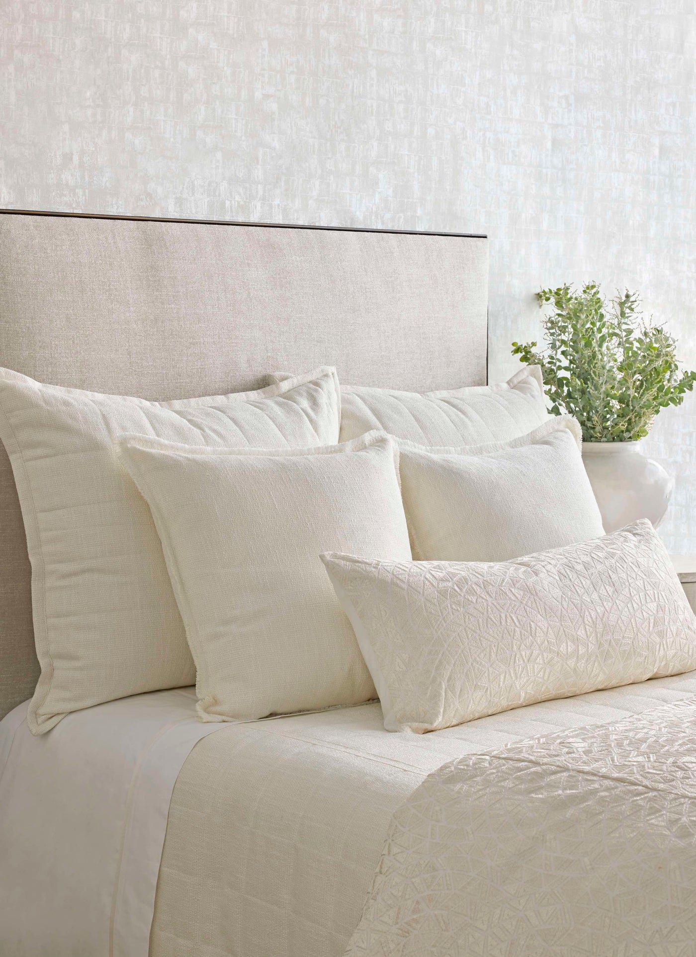 Ivory quilted bedding ensemble styled with layered pillow arrangement and eucalyptus accent.