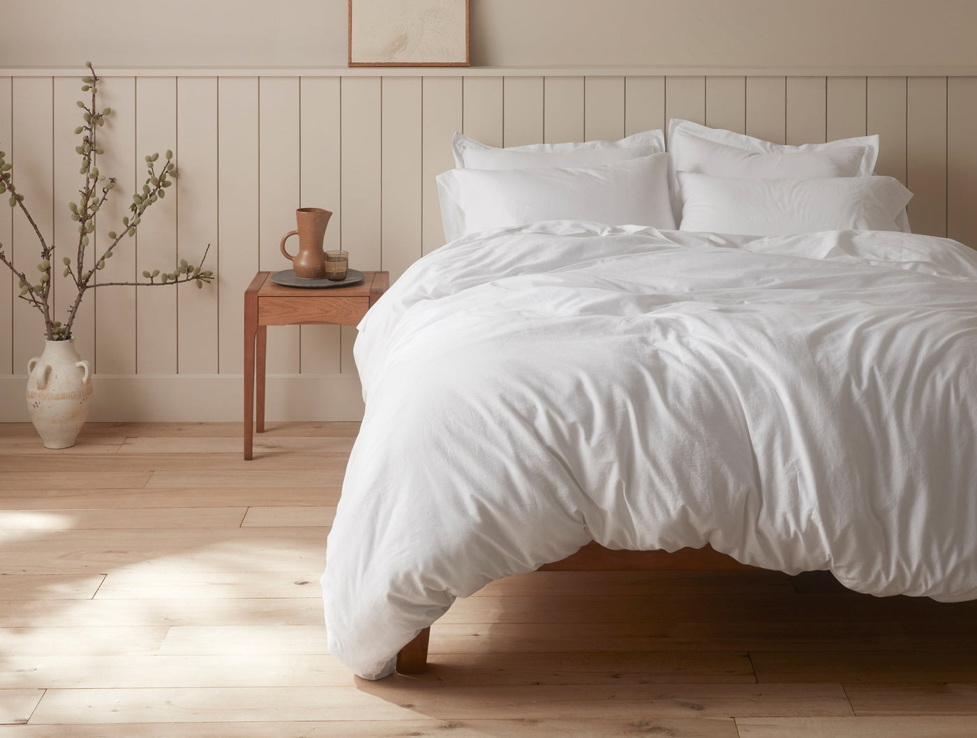 Coyuchi Cloud Soft Sateen duvet cover in white, draped on a bed in a warm, minimal bedroom.