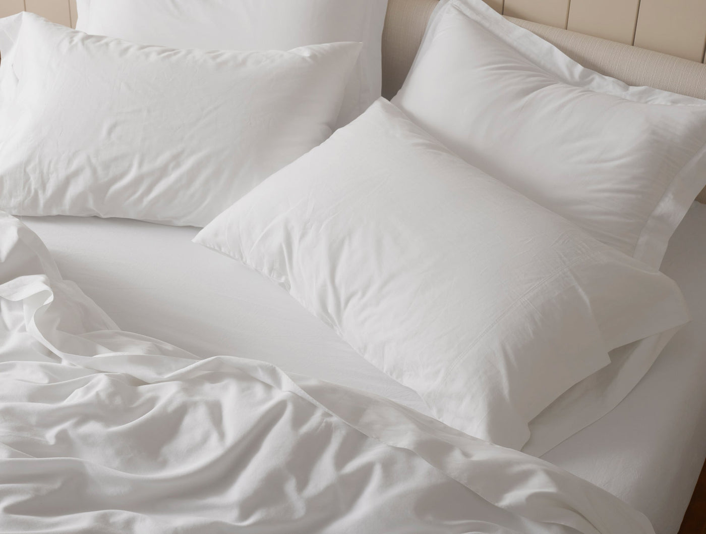 Rumpled white sateen duvet with layered pillows on a styled bed.