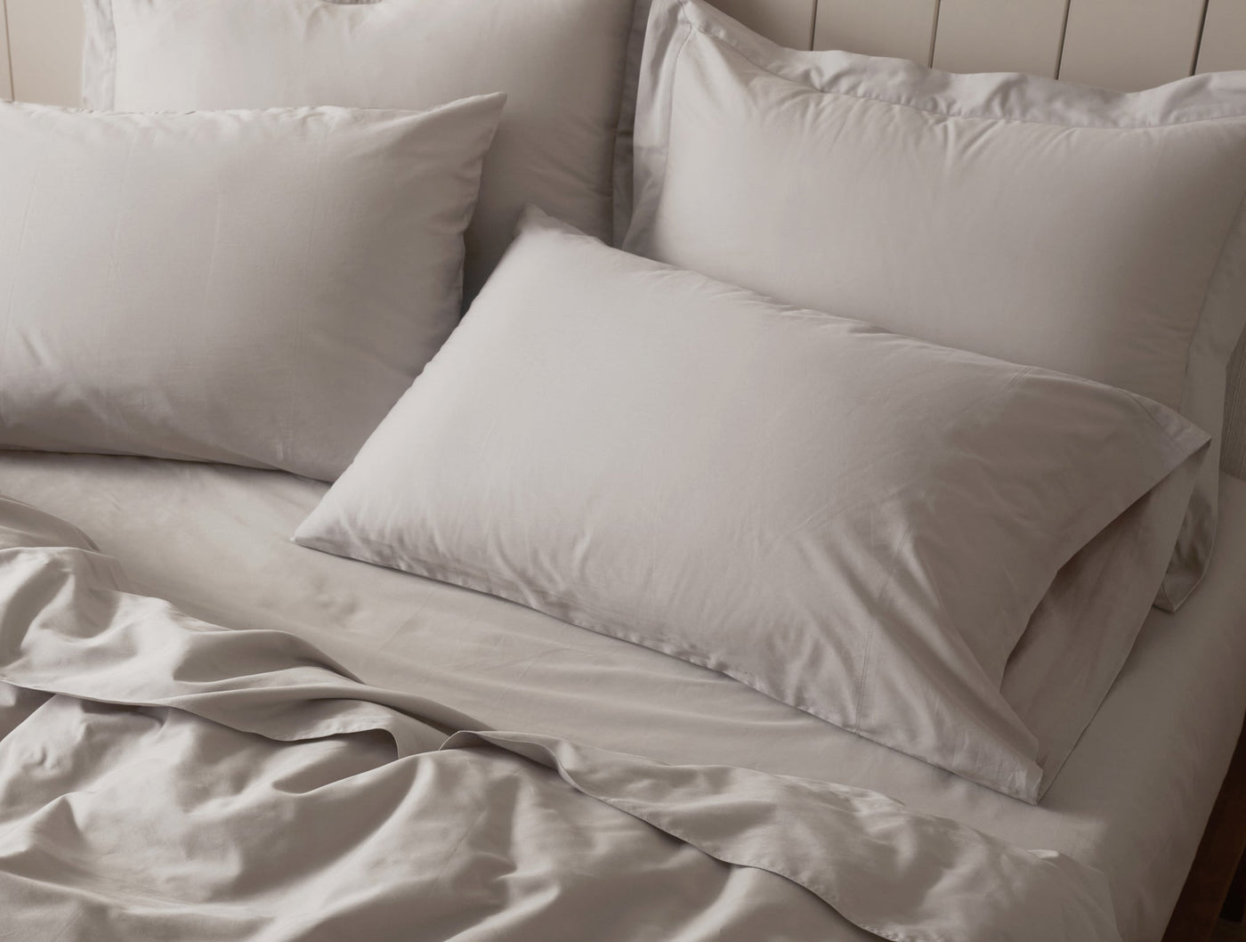 Relaxed silver sateen bedding styled on a bed with layered shams and rumpled duvet.