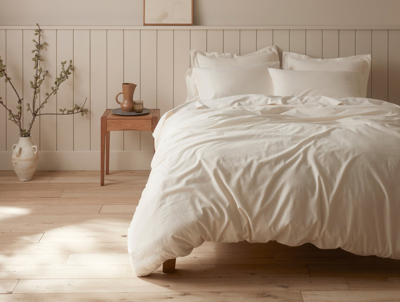 Ivory sateen duvet and shams styled on a sunlit bed in a warm, minimal bedroom.