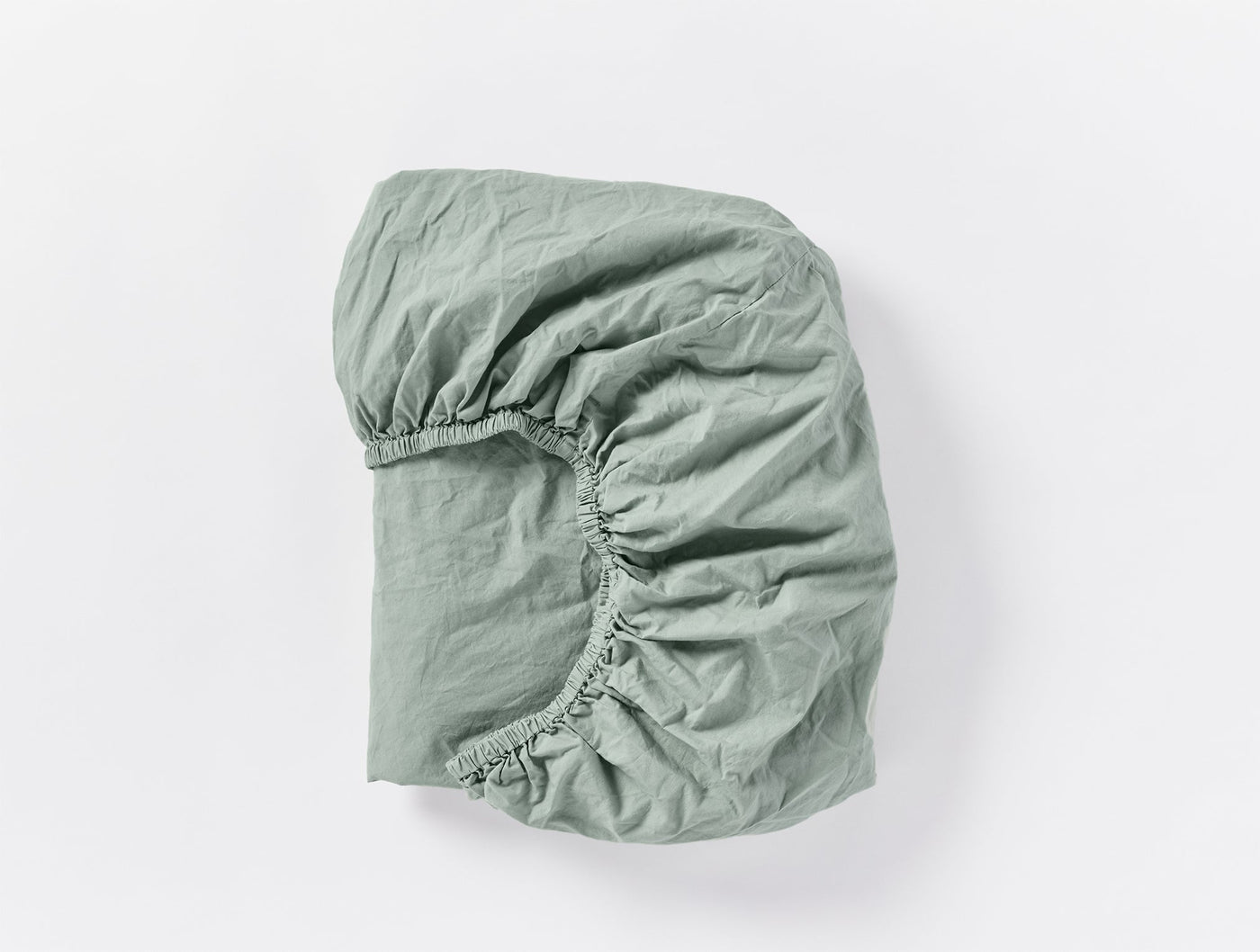 Sage green fitted sheet folded to show elasticized corner, crinkled percale texture visible.