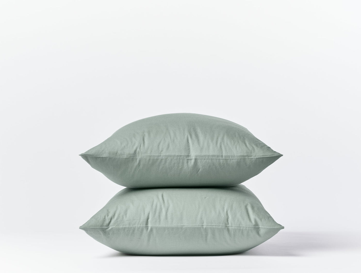 Two stacked sage Coyuchi Crinkled Percale pillowcases with subtle texture against white background.