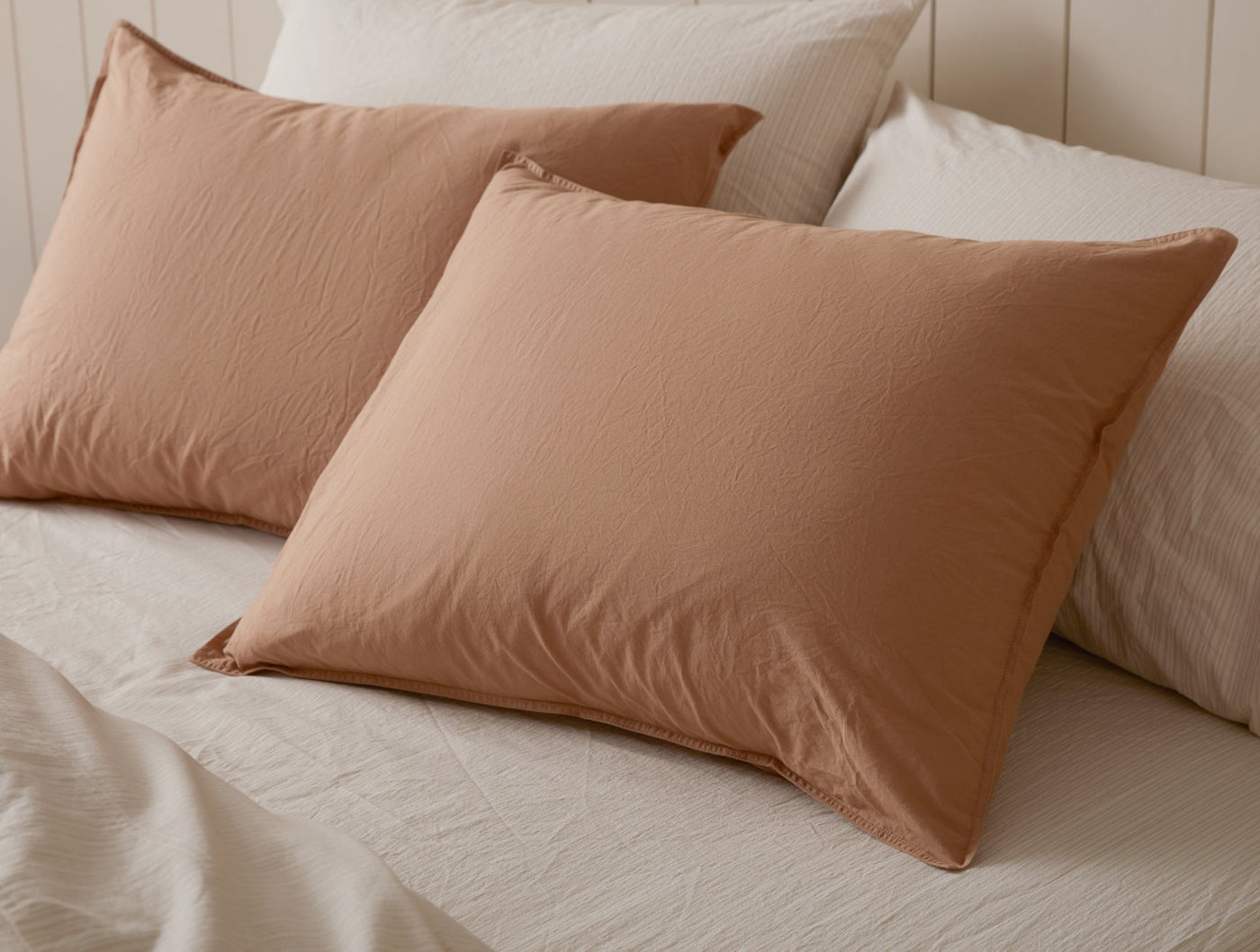 Two terracotta Coyuchi Crinkled Percale shams styled on a bed with white bedding.