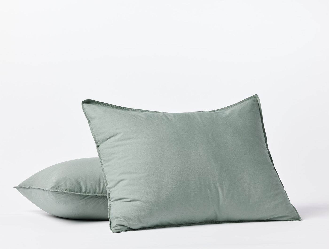 Close-up of two sage Coyuchi Crinkled Percale pillow shams stacked on white background.