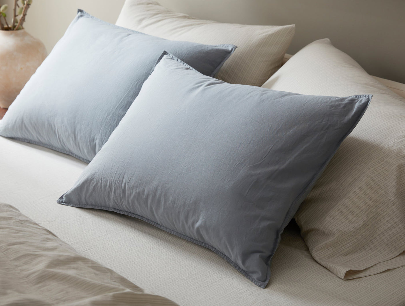 Close-up of two slate blue Coyuchi Crinkled Percale shams stacked on a made bed.