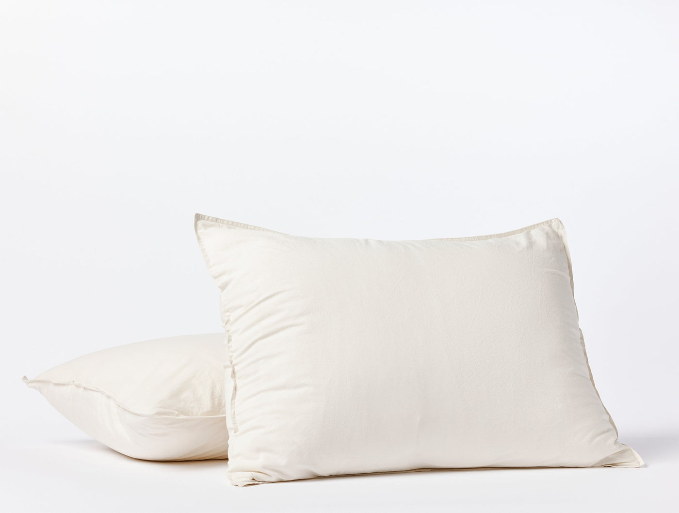 Close-up of two ivory Coyuchi Crinkled Percale pillow shams stacked against white background.