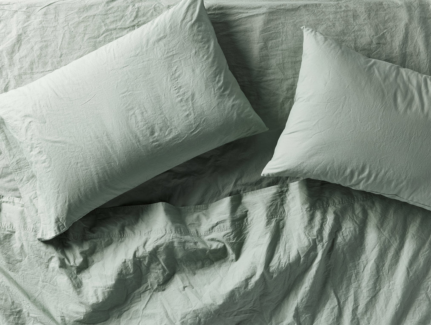 Close-up overhead view of two sage Coyuchi Crinkled Percale pillowcases with relaxed texture.