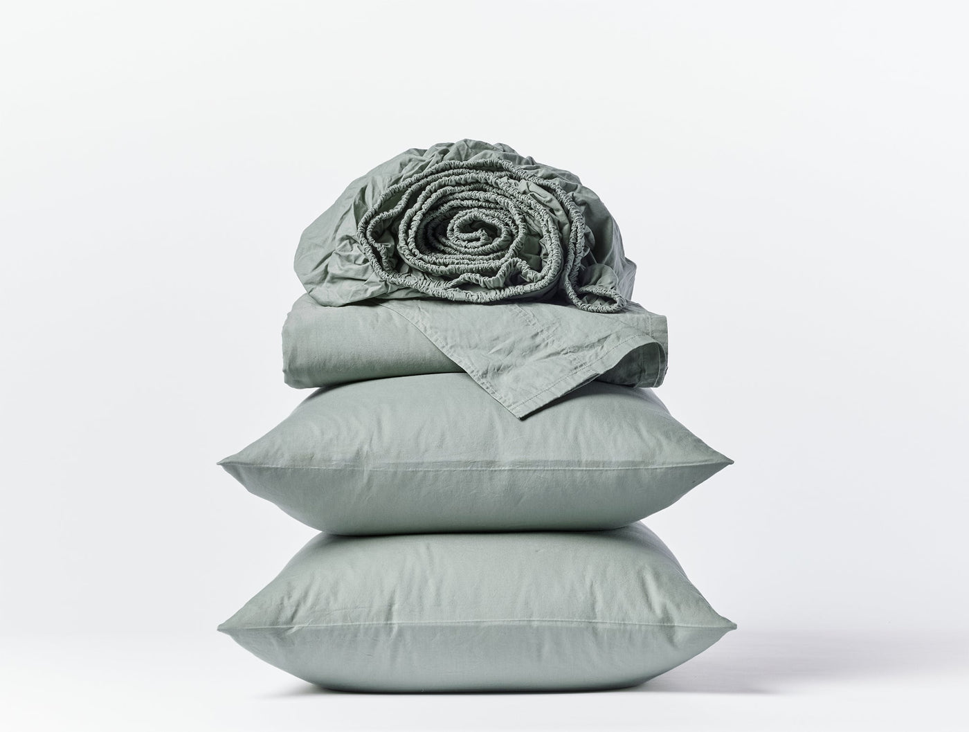 Sage green Coyuchi Crinkled Percale sheet set stacked with rolled fitted sheet on top.