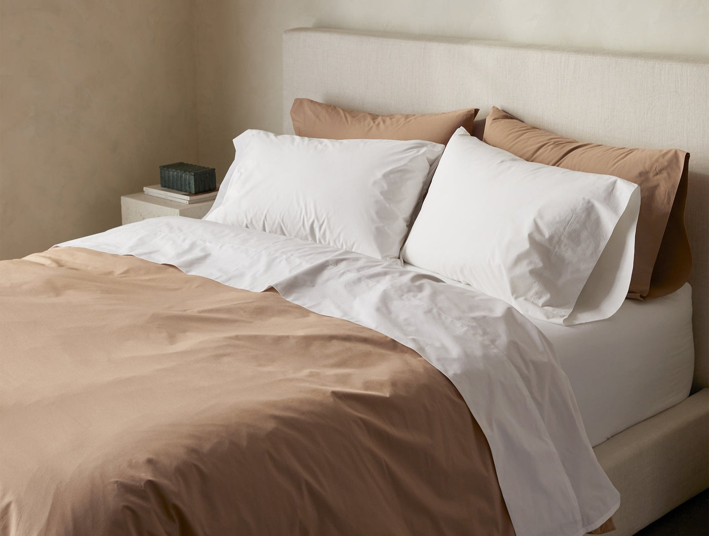 White percale pillowcases on a made bed with caramel duvet, angled bedroom view.