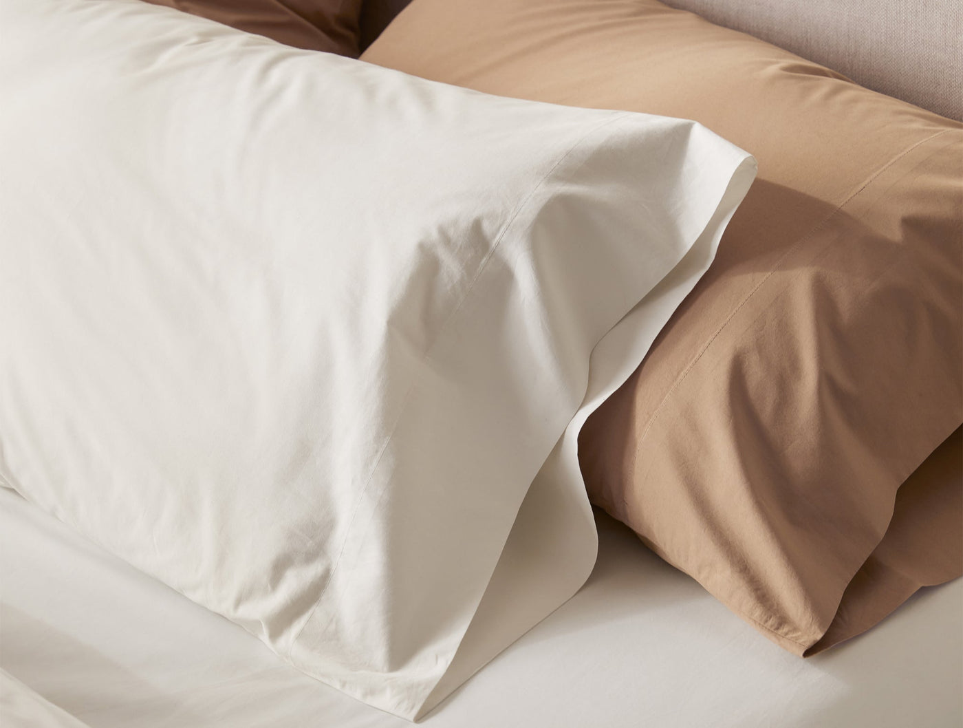 Ivory and dune percale pillowcases layered on a made bed, showing smooth finish.