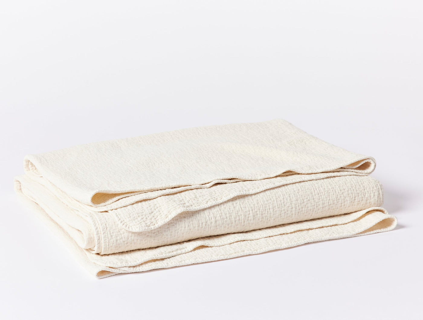 Coyuchi Cascade Matelassé blanket folded, showing ivory textured weave and scalloped edges.