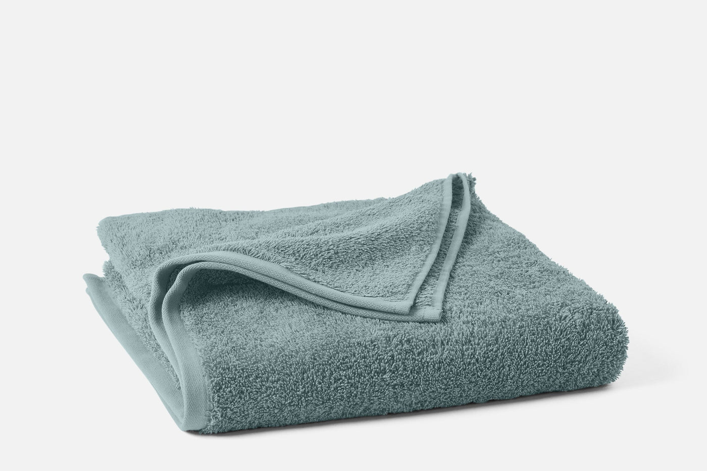 Coyuchi Cloud Loom towel folded in muted teal, showing plush loop texture and hem detail.