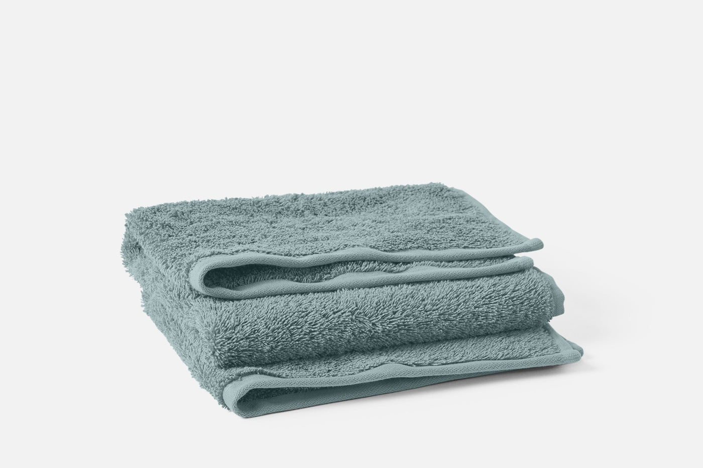 Folded seafoam terry towels stacked, showing plush loop texture and smooth hem detail.