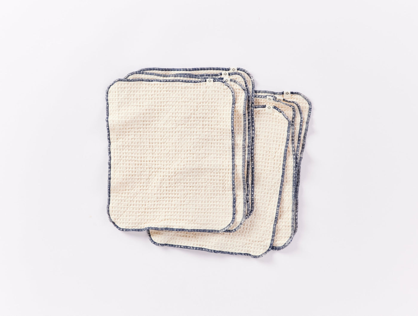 Close-up of stacked ivory Coyuchi paperless towels with navy blue contrast edge stitching.