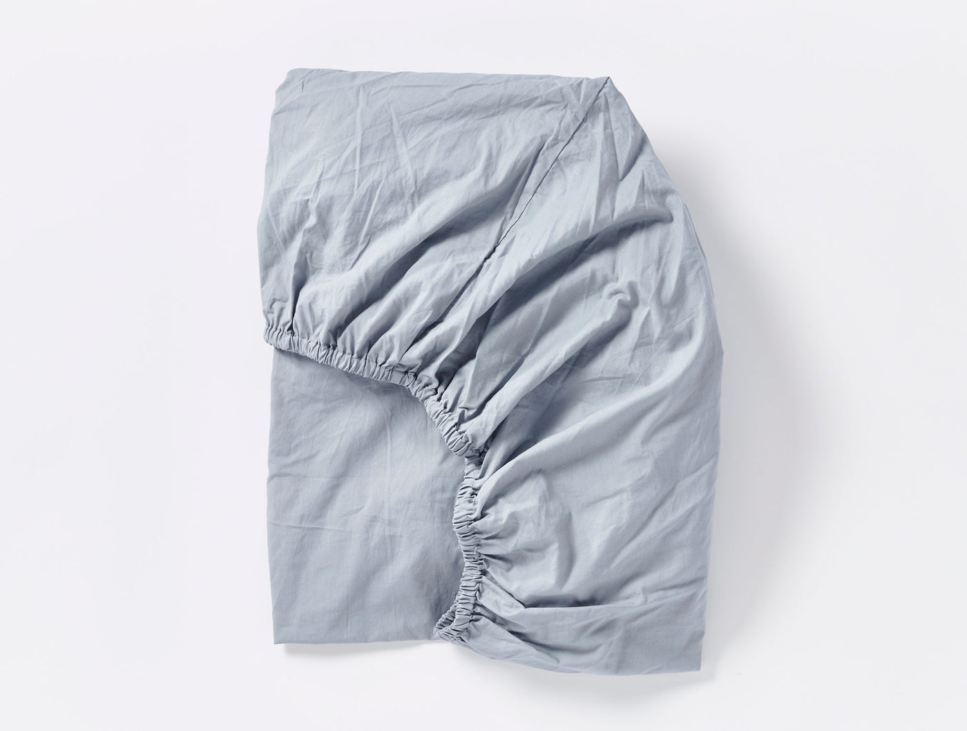 Slate blue fitted sheet folded to show elasticated corners and crinkled percale texture.