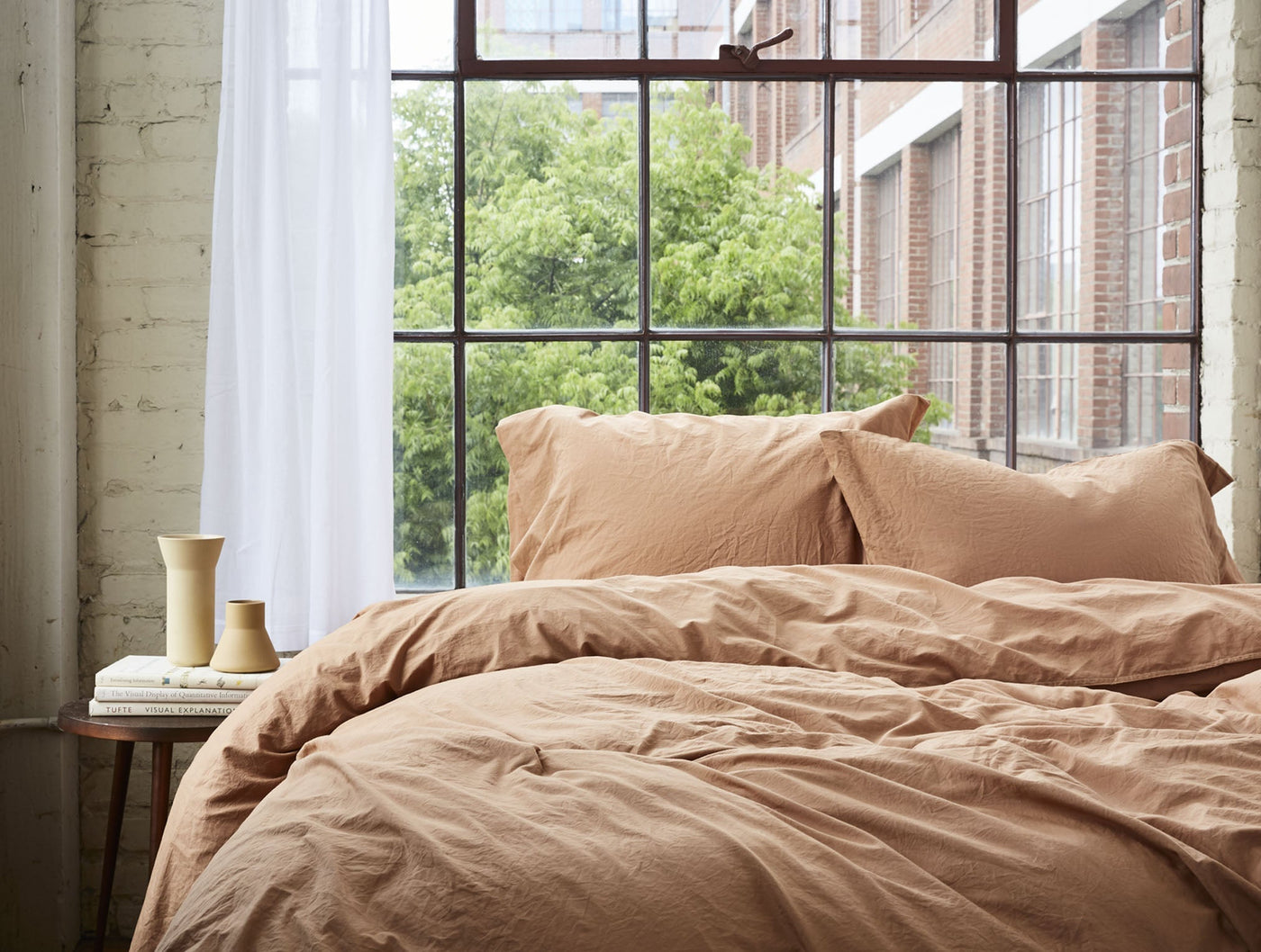Coyuchi Crinkled Percale pillowcases in terracotta, styled on a made bed near a window.