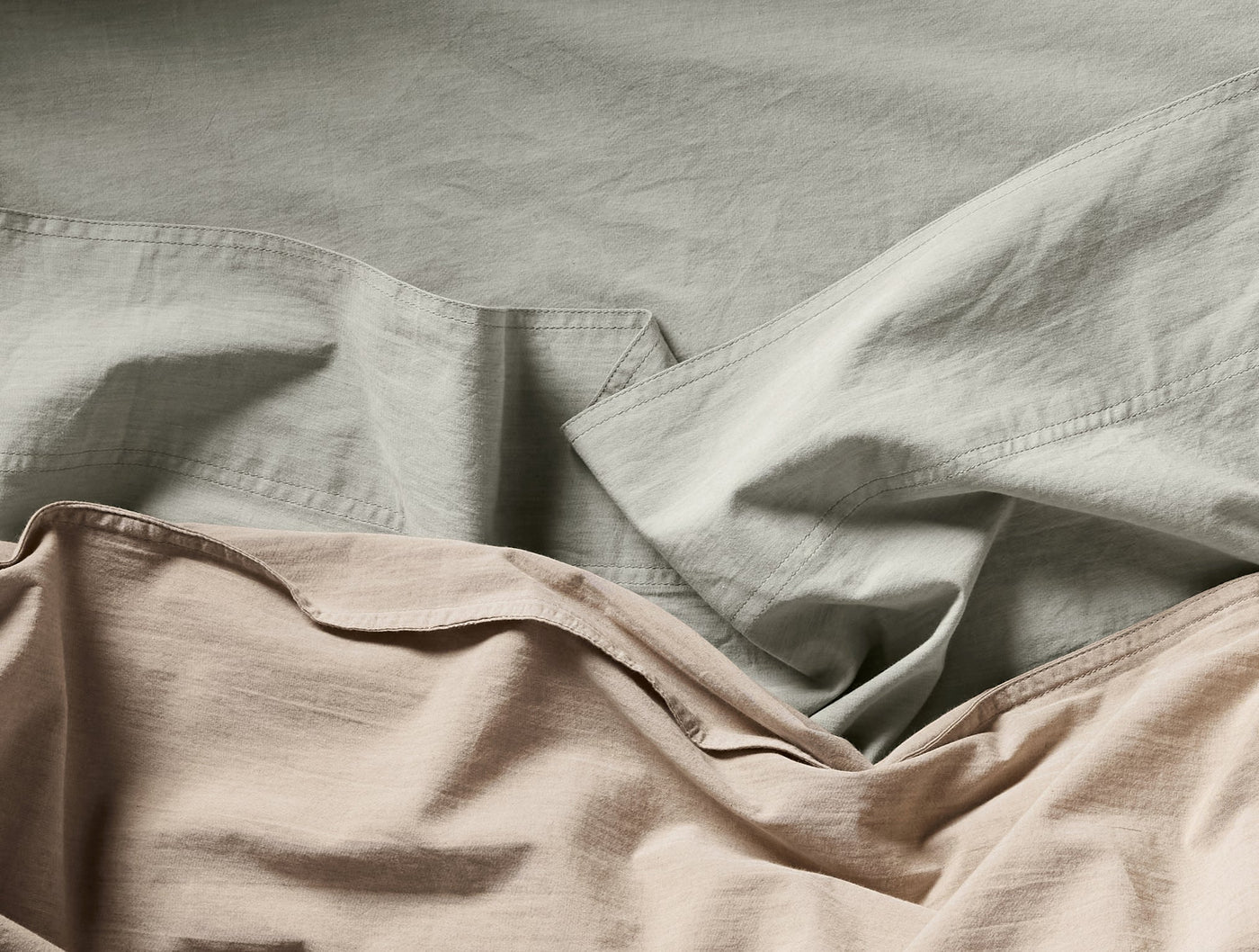Close-up of sage and dune Coyuchi Crinkled Percale sheets layered with visible texture.