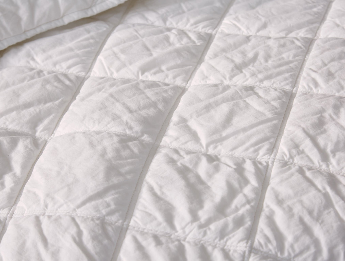 Close-up of Coyuchi diamond-stitched white cotton comforter showing quilted texture detail.