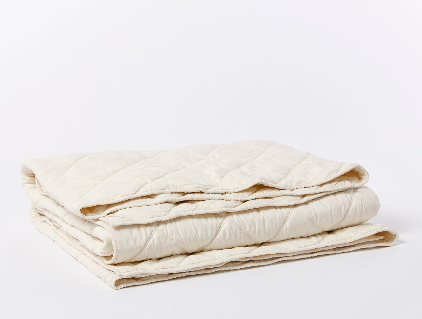 Ivory quilted comforter folded, showing diamond-stitch pattern and natural cotton texture.