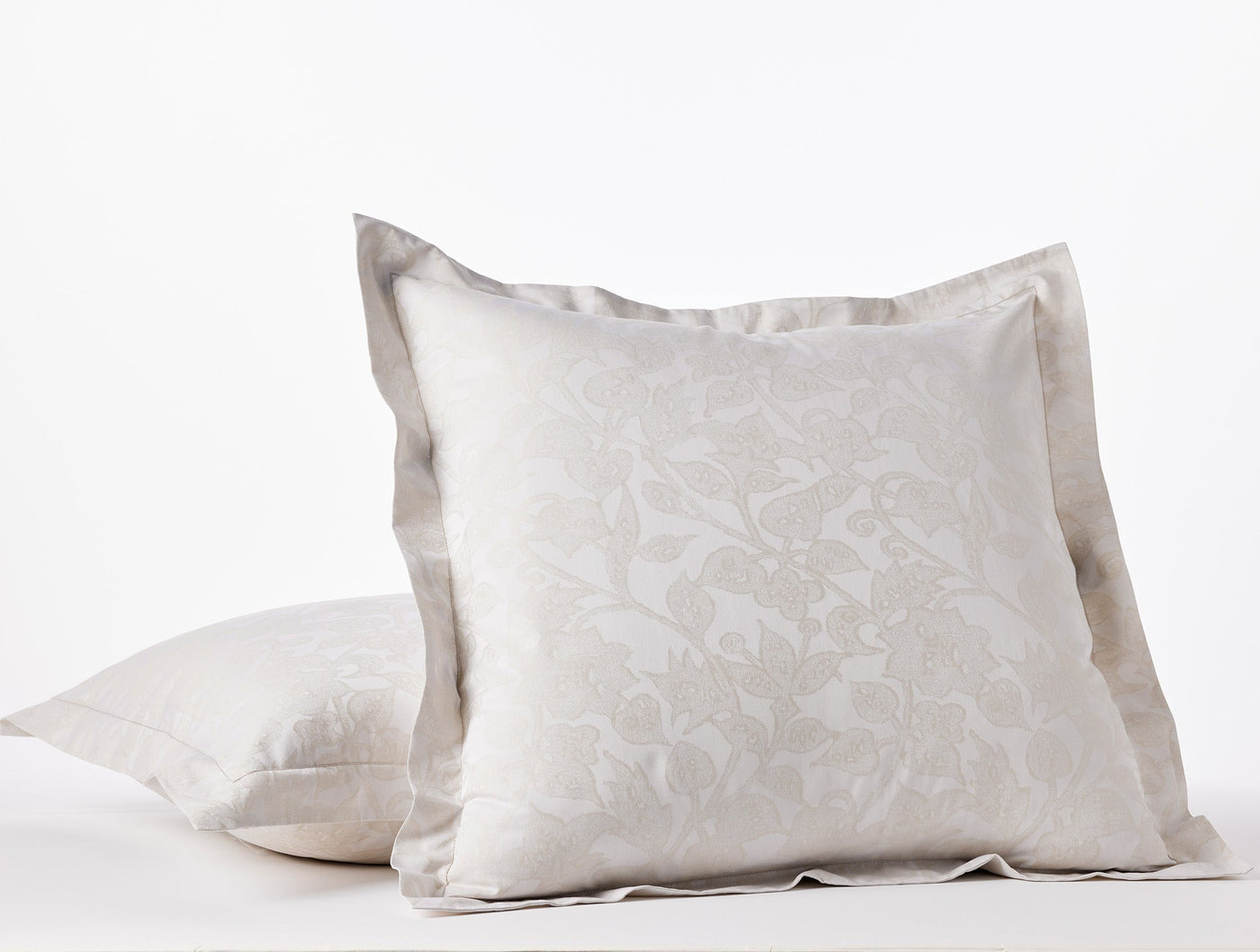 Angled view of two stacked ivory Coyuchi Heritage Percale Jacquard shams with flange border.