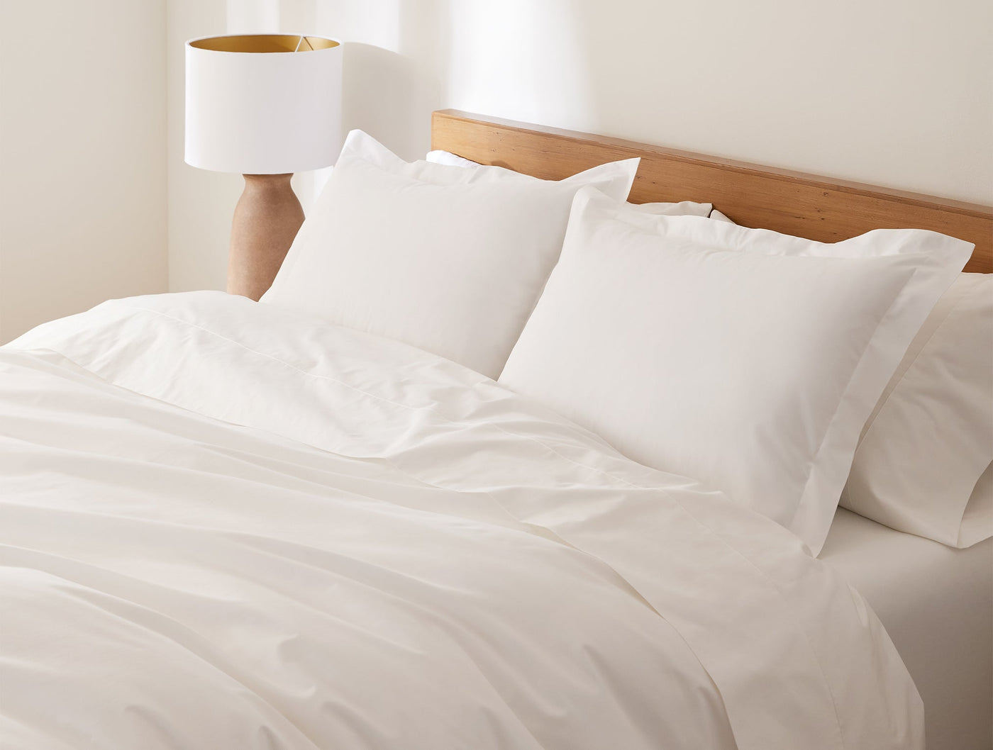 Close-up of Coyuchi Heritage Percale shams in white, styled on a made bed with layered pillows.