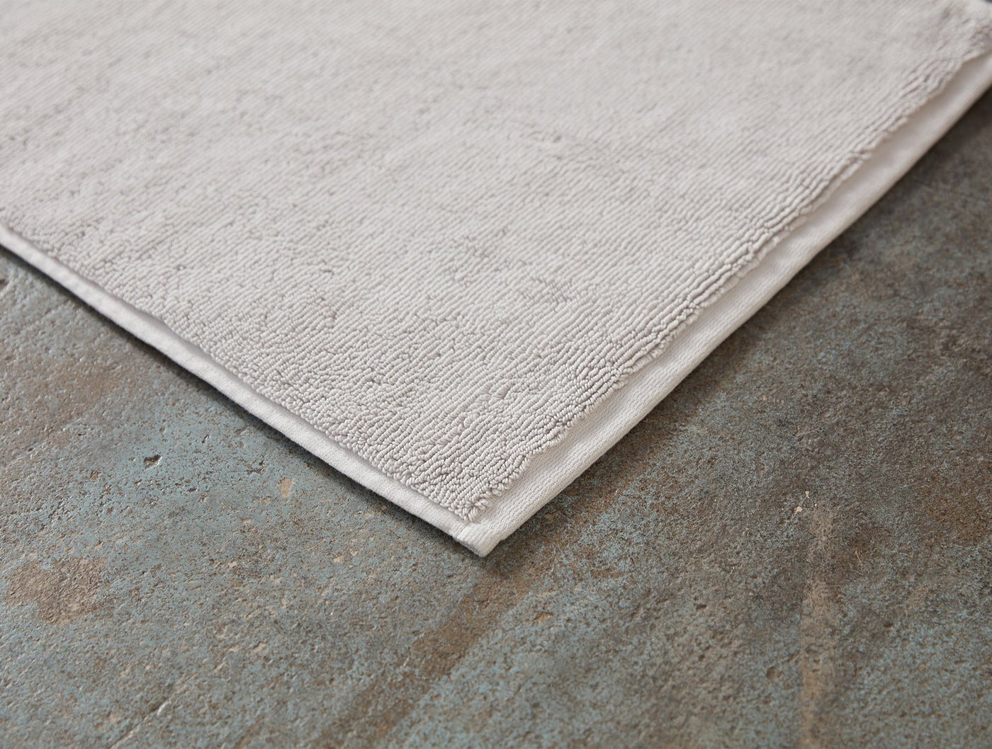 Corner detail of an ivory Coyuchi Cloud Loom bath rug showing ribbed texture and woven border edge.