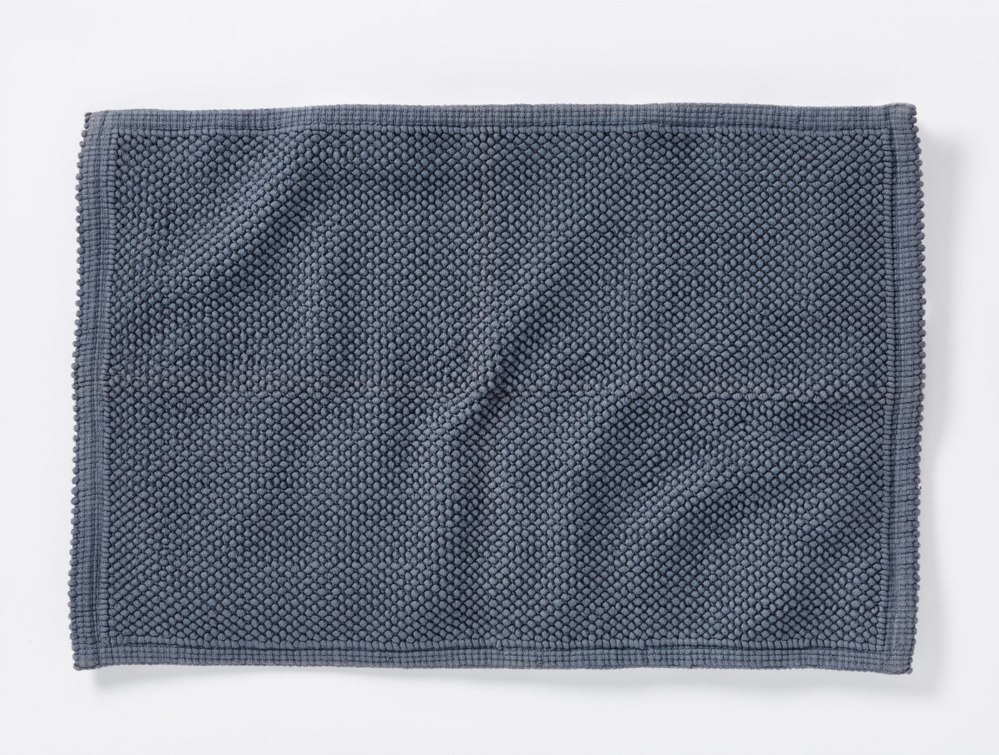 Coyuchi Pebbled bath rug in slate blue, overhead view showing textured weave and border detail.