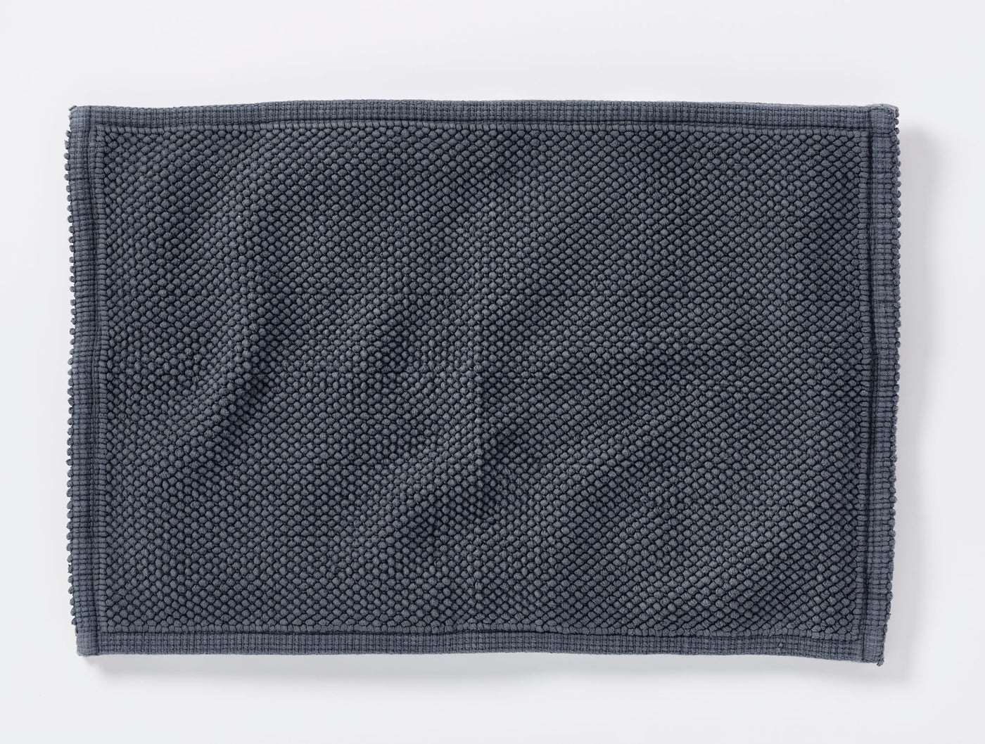 Coyuchi Pebbled bath rug in slate blue, overhead view showing textured weave and border trim.