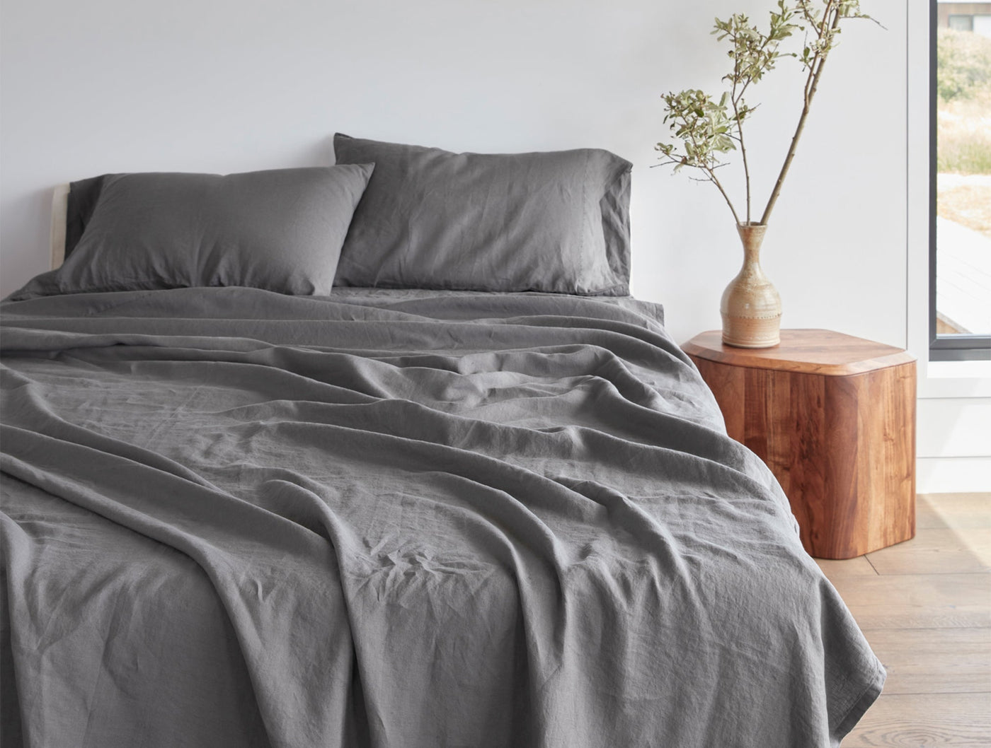 Coyuchi Relaxed Linen fitted sheet in charcoal, styled on a bed with matching pillowcases.