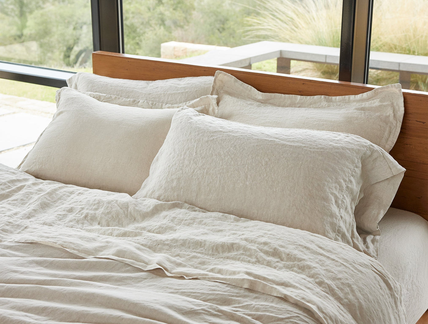 Oatmeal linen pillowcases styled on a made bed with natural light and garden views.