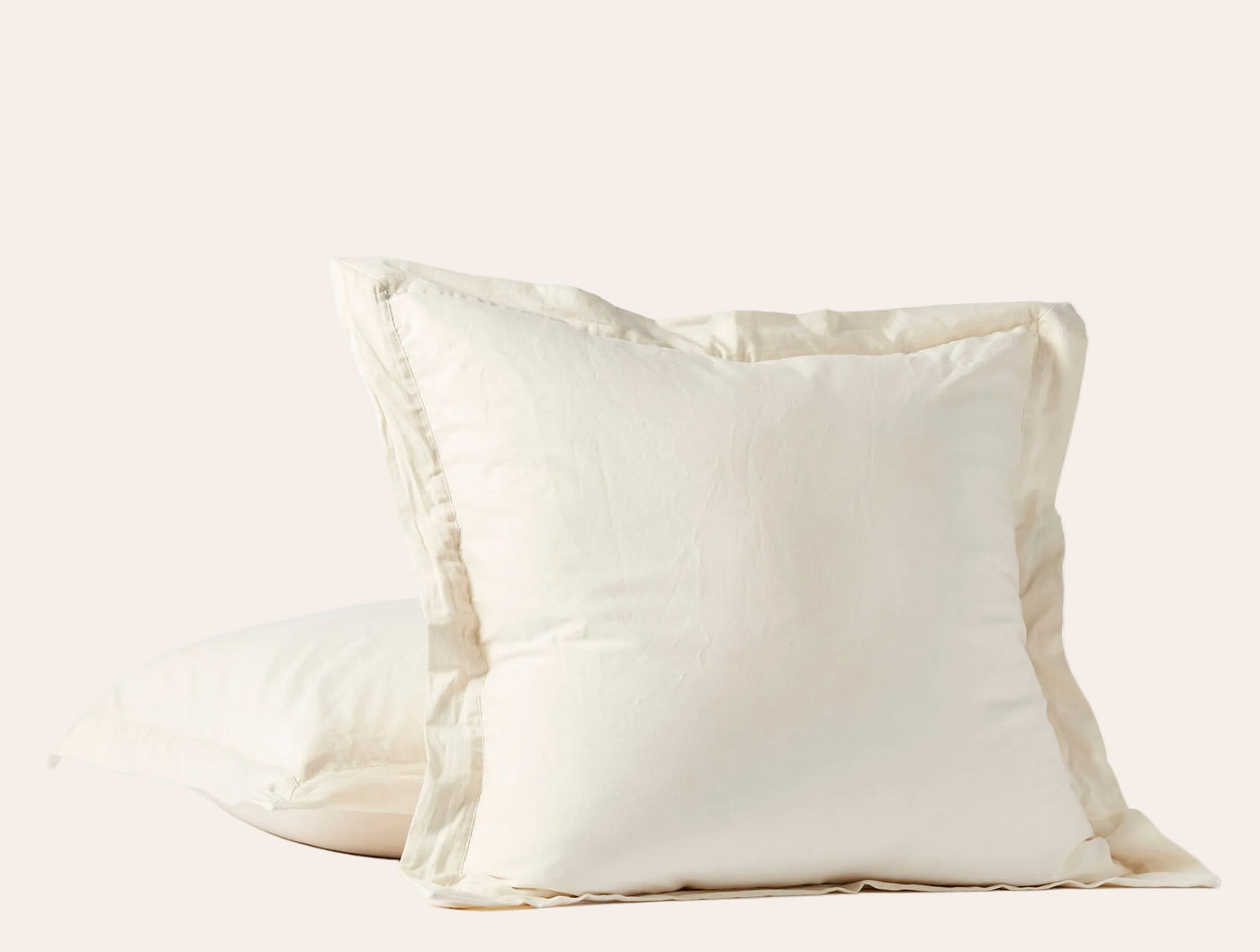 Close-up of two ivory Coyuchi Cloud Soft Sateen pillow shams stacked, showing flange edge detail.