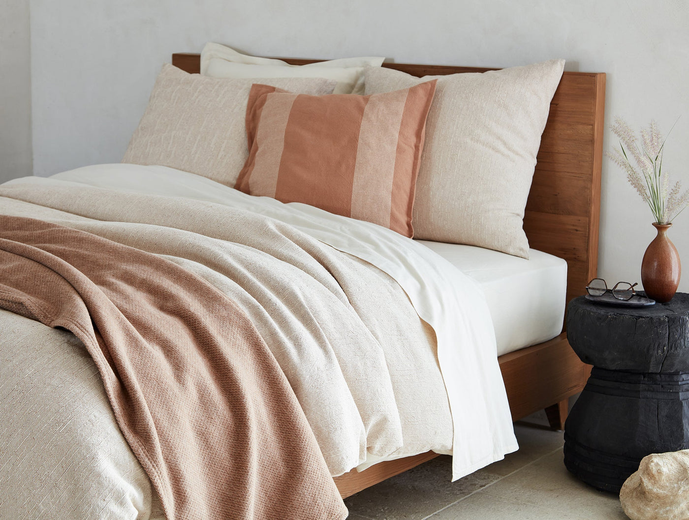 Ivory textured blanket draped over bed with terracotta accents and warm wood headboard.