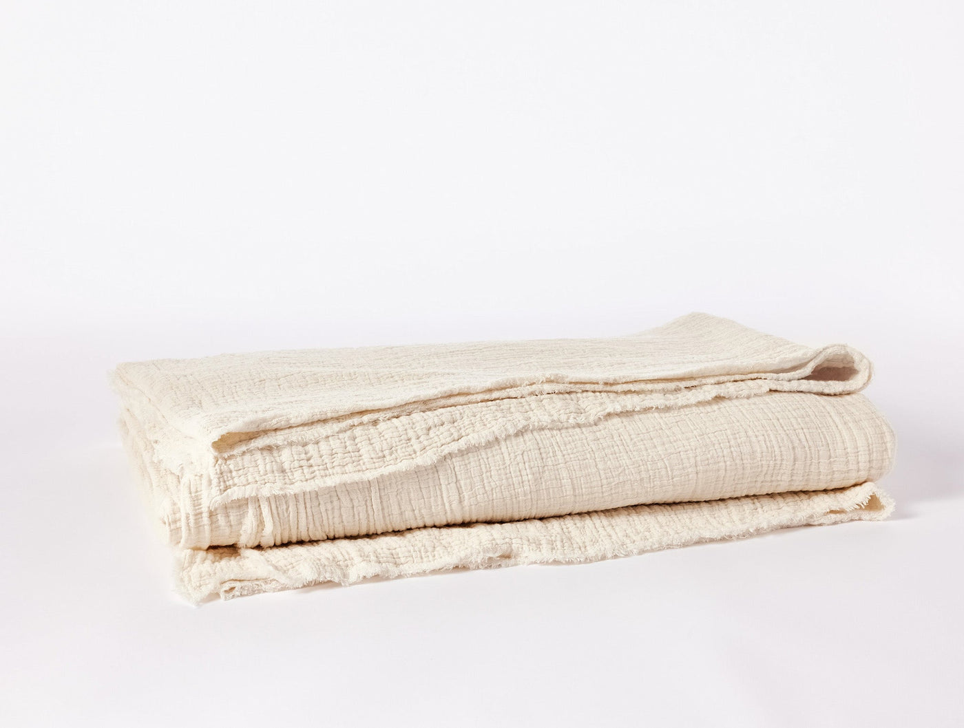 Folded ivory Coyuchi Topanga Matelassé blanket showing textured weave and fringe edge detail.
