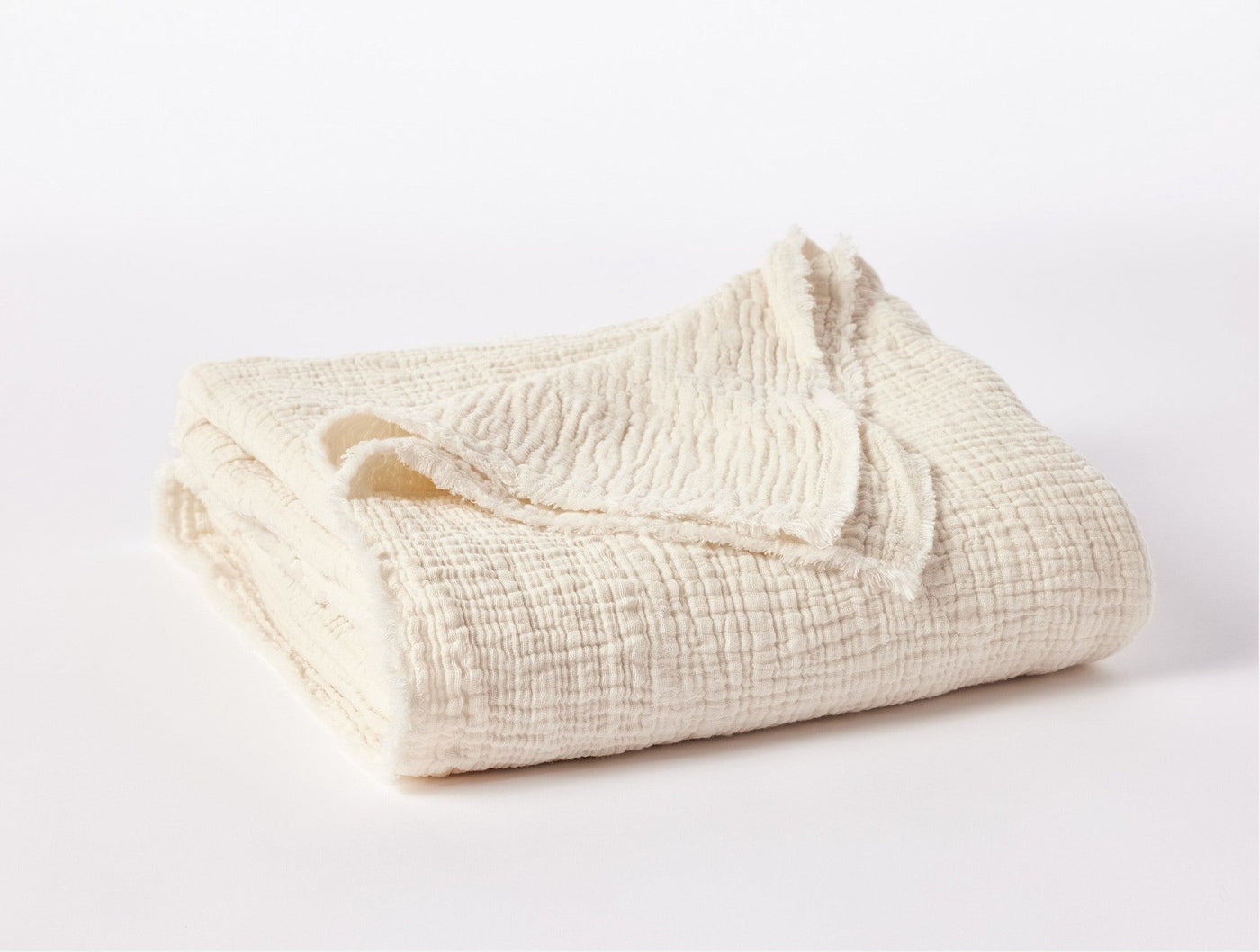 Ivory matelasse throw folded to show crinkled texture and fringe edge detail.