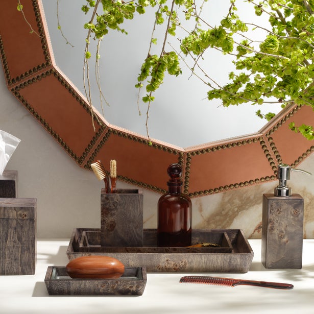 Dark marble-finished bathroom accessories set styled on vanity with mirror and greenery.