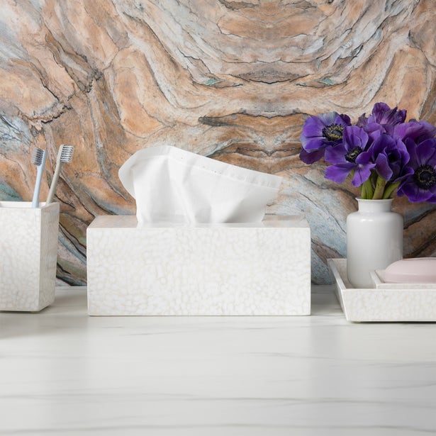 White crackle-textured bath accessories set styled on white surface with marble wall and purple flowers.