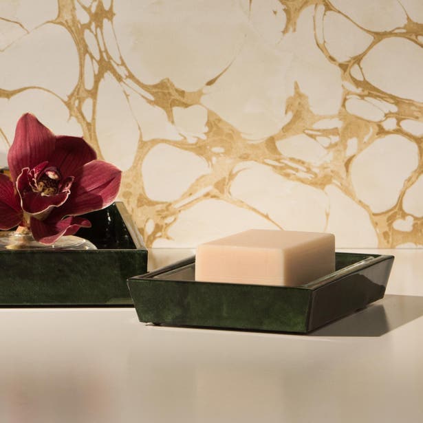 Dark green marbled soap dish holding a bar of soap, styled with orchid blooms against gold-veined wall.