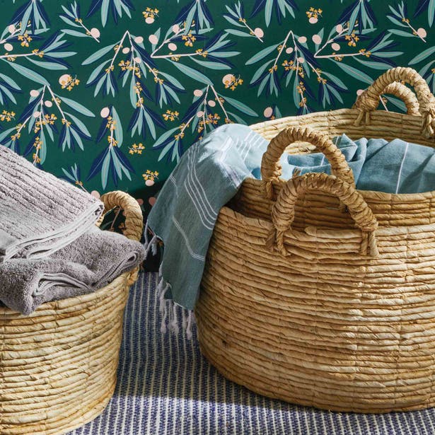 Pigeon & Poodle Clio woven basket set with linen throws, styled against floral wallpaper.