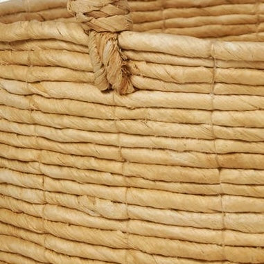 Close-up of Clio basket's natural raffia coiled weave and knotted rope handle detail.