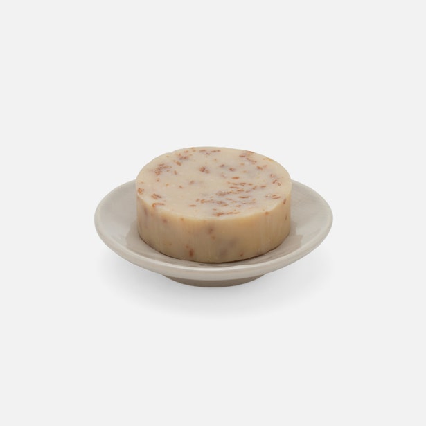 Round ivory soap bar with red speckles resting on a Pigeon & Poodle Cordoba soap dish.