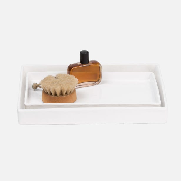 White lacquered nesting trays styled with a brush and amber glass bottle on a light background.