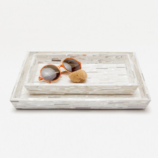 Stacked ivory mother-of-pearl mosaic bath trays styled with sunglasses and a stone object.