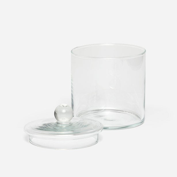 Clear glass Darby bath canister with round knob lid resting beside it.